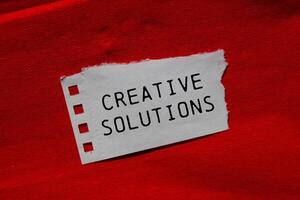 Creative solutions message written on ripped torn paper piece on red background. Conceptual creative solutions symbol. Copy space. photo
