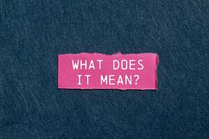 What does it mean question written on ripped pink torn paper piece on gray background. Conceptual what does it mean question symbol. Copy space. photo