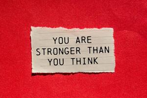 You are stronger than you think message written on ripped torn paper piece on red background. Conceptual you are stronger than you think symbol. Copy space. photo