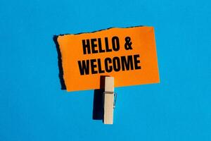 Hello and welcome message written on ripped torn orange paper on blue background. Conceptual hello and welcome symbol. Copy space. photo