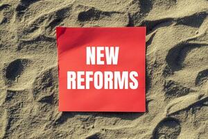 New reforms message written on red paper with beach sands background. Conceptual new reforms symbol. Copy space. photo