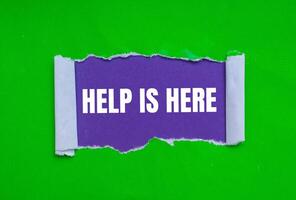 Help is here message written on ripped torn green paper on purple background. Conceptual help is here symbol. Copy space. photo