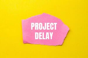 Project delay message written on ripped torn pink paper piece with yellow background. Conceptual project delay symbol. Copy space. photo