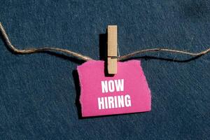 Now hiring message written on ripped torn pink paper piece with gray background. Conceptual now hiring symbol. Copy space. photo