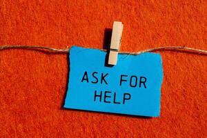Ask for help message written on ripped blue torn paper piece on orange background. Conceptual ask for help symbol. Copy space. photo