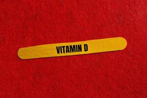 Vitamin d message written on yellow wooden stick with red background. Conceptual vitamin d symbol. Copy space. photo