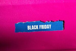 Black friday message written on ripped torn blue paper piece with pink background. Conceptual black friday symbol. Copy space. photo