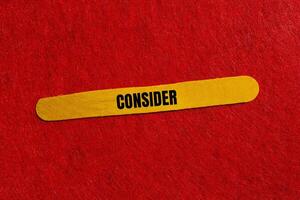 Consider message written on yellow wooden stick with red background. Conceptual consider symbol. Copy space. photo