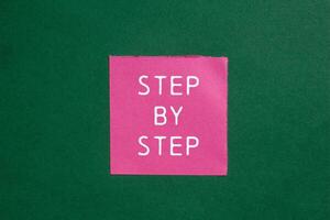 Step by step message written on ripped torn pink paper on green background. Conceptual step by step symbol. Copy space. photo