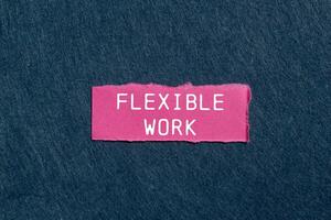 Flexible work message written on ripped pink torn paper piece on gray background. Conceptual flexible work symbol. Copy space. photo