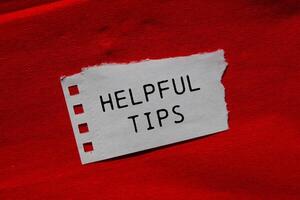 Helpful tips message written on ripped torn paper piece on red background. Conceptual helpful tips symbol. Copy space. photo