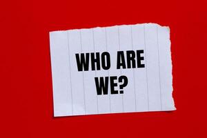 Who are we question written on ripped torn paper piece with red background. Conceptual who are we question symbol. Copy space. photo