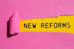 New reforms message written on ripped torn pink paper with yellow background. Conceptual new reforms symbol. Copy space. photo