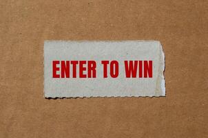 Enter to win message written on ripped torn paper piece with cardboard background. Conceptual enter to win symbol. Copy space. photo
