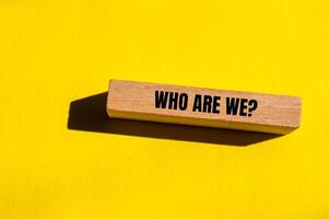 Who are we question written on wooden block with yellow background. Conceptual who are we question symbol. Copy space. photo