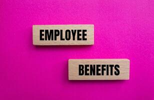 Employee benefits message written on wooden blocks with pink background. Conceptual employee benefits symbol. Copy space. photo