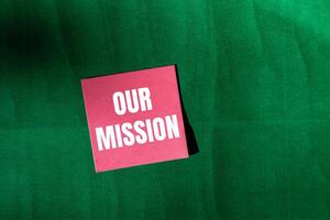 Our mission message written on pink paper with green background. Conceptual our mission symbol. Copy space. photo