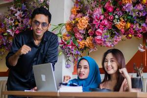 Group of Asian students happy looking at camera successfully solve complicated case from lecturer in front of laptop computer in coffee shop cafe. for group concept, company, education, education photo