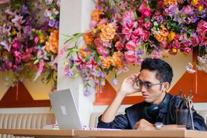 Asian handsome man student weak head dizzy thinking about assignment in front of laptop computer on the table, sitting in cafe workplace. for health, education, technology, lifestyle content photo