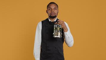Catering staff waiter doing a mute sign for silence and privacy, keeping quiet while he carries cruet set with condiments for customer satisfaction. Shows a hush symbol to keep secret. Camera B. photo