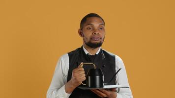 Restaurant staff serving clients with tea before their dinner order, bringing the teapot at the table. Waiter dressed in apron serves customers for satisfaction, service oriented industry. Camera A. photo