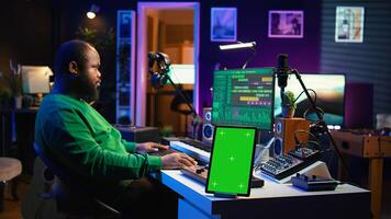 Composer editing his audio files and recordings on daw software, sitting next to a green screen display. Skilled sound technician uses mixing and mastering gear to produce new material. Camera B. photo
