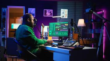 African american sound engineer using midi controller notes to add audio effects in post production, editing tracks with digital software and mixing console. Male musician in home studio. Camera B. photo