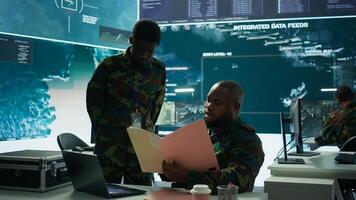 Angry army expert in a command post power base monitors satellite footage, yelling at soldier and throwing papers. Frustrated officer looks at real time data for operational success. Camera B. photo