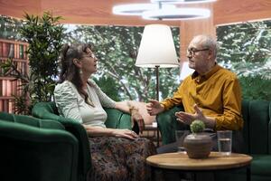 Senior husband and wife smiling and enjoying a cheerful conversation, feeling good in their free time and relaxing at home. Embracing aging process and longevity together with joy. photo