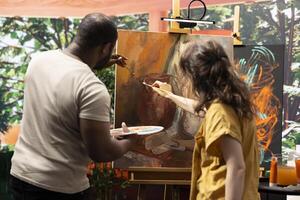 Diverse team of artists collaborating on a rustic colorful painting in art and craft workshop, mixing colors and applying them on a canvas. Two painters expressing their skill and creativity. photo
