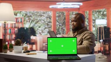 Small business owner works on finances plans next to a green screen, using annual sales analytics to increase startup profit. Entrepreneur does budget balance analysis at home desk. Camera B. photo