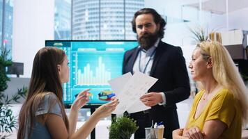 Financial advisor showing statistical graphs on big screen to customers, analyzing market trends to optimize income. Family members checking investment plan on display made by consultant, camera A photo