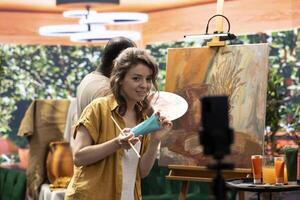 Female artist explaining the painting techniques used on online tutorial, recording a vlog for art class to teach people how to paint with watercolor on canvas. Team of painters do content creation. photo