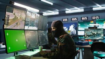 Masked intelligence corps agent overseeing national safety operations with mockup equipment. Special forces spy examining data in monitoring room with chroma key monitors, camera B photo