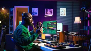 Male composer recording his melody on microphone in home studio, singing a song of his own creation. Talented artist using audio files and lyrics to apply mixing and mastering techniques. Camera B. photo