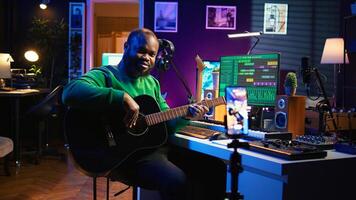 Guitarist instructor hosting guitar lessons online using a mobile phone, recording tutorial for master class. Artist musician explains acoustic instrument accords, assistance for beginners. Camera B. photo