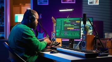 Confident music composer mixing sounds on digital audio software, creating a cool atmosphere in his home studio. Young cheerful producer composing new soundtracks with stereo gear. Camera A. photo