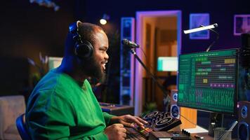 Young musician twisting knobs and mixing tunes with a console, following record settings on a digital software interface. Artist composer producing new music hits in his home studio. Camera B. photo
