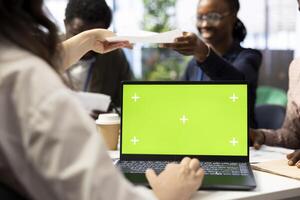 CEO uses laptop with green screen during a meeting with business associates, reviewing project development progress. Utilizing detailed analytics and mockup to ensure strategic objectives. photo
