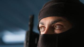 Terrorist hiding identity, attacking enemy command center. Close up of masked insurgent inspecting room during enemy base assault hijacking in guerilla warfare armed conflict, camera A photo