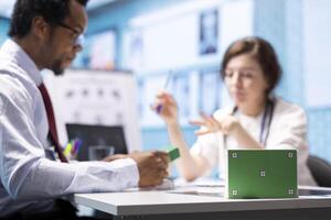 Patient and general practitioner in a consultation next to green screen on medicine box, discussing about treatment pills and supplements for wellness. Specialist pointing at medicaments. photo
