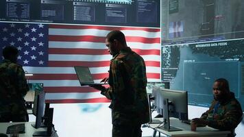Professionals in US military uniforms operate computers and big screen, working on surveillance and intelligence to ensure national security from a high tech control center. Camera B. photo