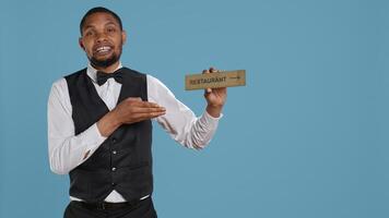 Doorman bellhop showing the restaurant direction with a hotel sign, holding an indicator to point guests to the amenities. Professional hotel concierge using a wall mark. Camera B. photo