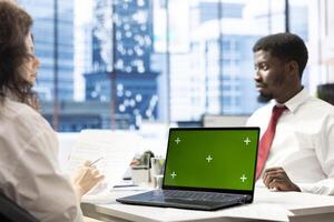 HR specialist using green screen laptop to reviewing candidate CV, asking questions about qualifications. Person getting hired by recruiter using chroma key notebook after proving skills for job photo