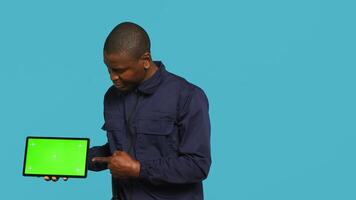 Portrait of smiling security guard at work showcasing isolated screen tablet while overseeing premises. Joyful private law enforcement worker presenting chroma key device, studio backdrop, camera A photo