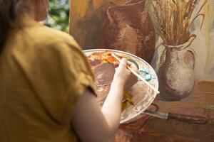 In a rustic workshop, artist mixes a variety of watercolor paint on a palette to create a colorful masterpiece on canvas. Woman painting with a brush and showing her skill, artwork creation. photo
