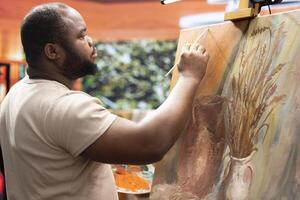 Focused man painting a new rustic artwork on canvas with brushstrokes patterns, mixing watercolors and applying to create a masterpiece. Young male artist working on his creation. photo