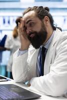 General practitioner feeling tired and stressed after analyzing medical records and test results, ensuring recovery in treatment center. Physician working under pressure to find a cure for illness. photo