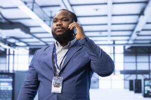 Supervisor discussing on mobile phone in high tech data center housing advanced computing hardware. Professional delegating tasks in futuristic server farm during telephone call photo