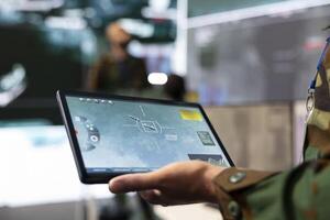 Army IT professional employing a satellite world map with location tracking system on his tablet, monitoring CCTV surveillance in military command post. Reconnaissance mission. Close up. photo